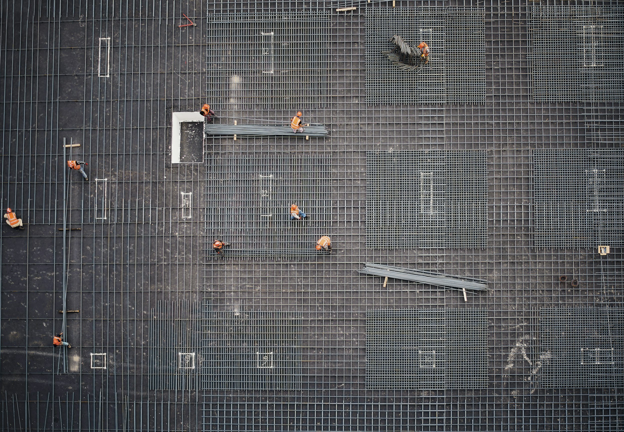 Construction workers in orange vests and hard hats installing metal grates on a building's rooftop.